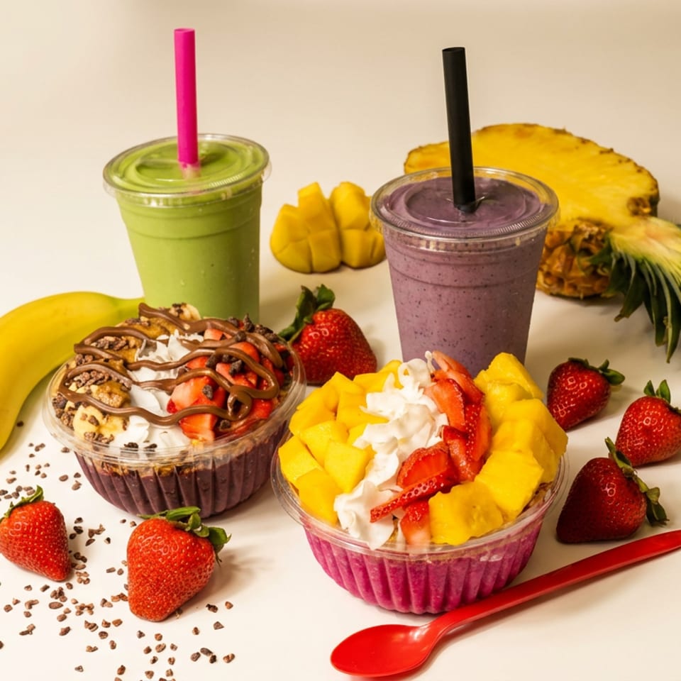 Fruit smoothies and açai bowls topped with mango, strawberries, coconut, and chocolate drizzle, surrounded by fresh fruit.
