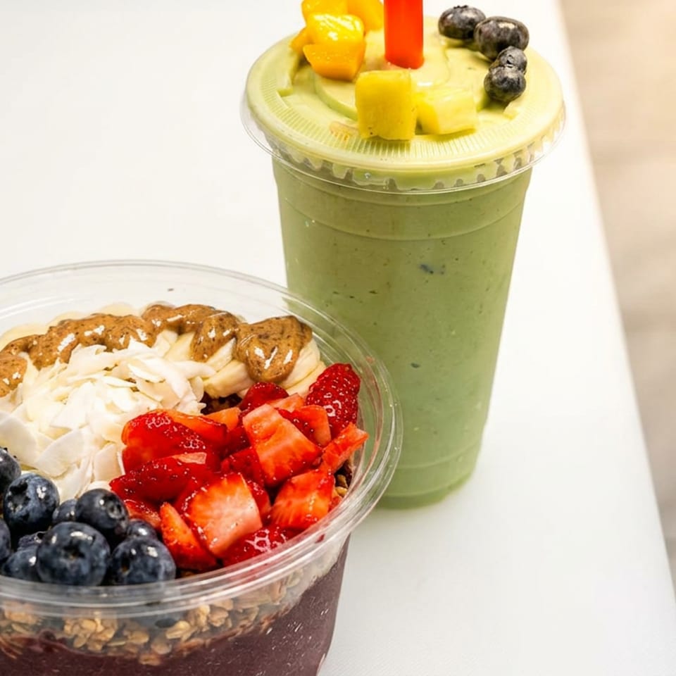 Acai bowl topped with blueberries, strawberries, coconut, banana, and nut butter beside a green smoothie topped with fruit.