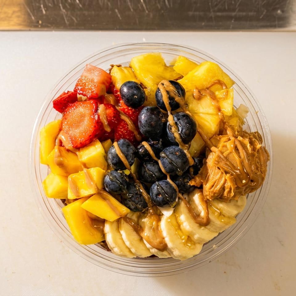 Fruit bowl topped with strawberries, mango, blueberries, banana slices, shredded coconut, and peanut butter drizzle.