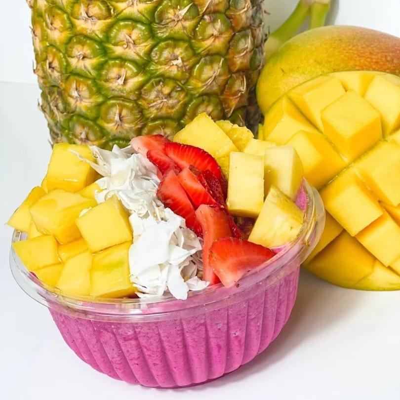 Vytal Nutrition smoothie bowl with mango, pineapple, strawberries, and coconut flakes, next to whole fruits.
